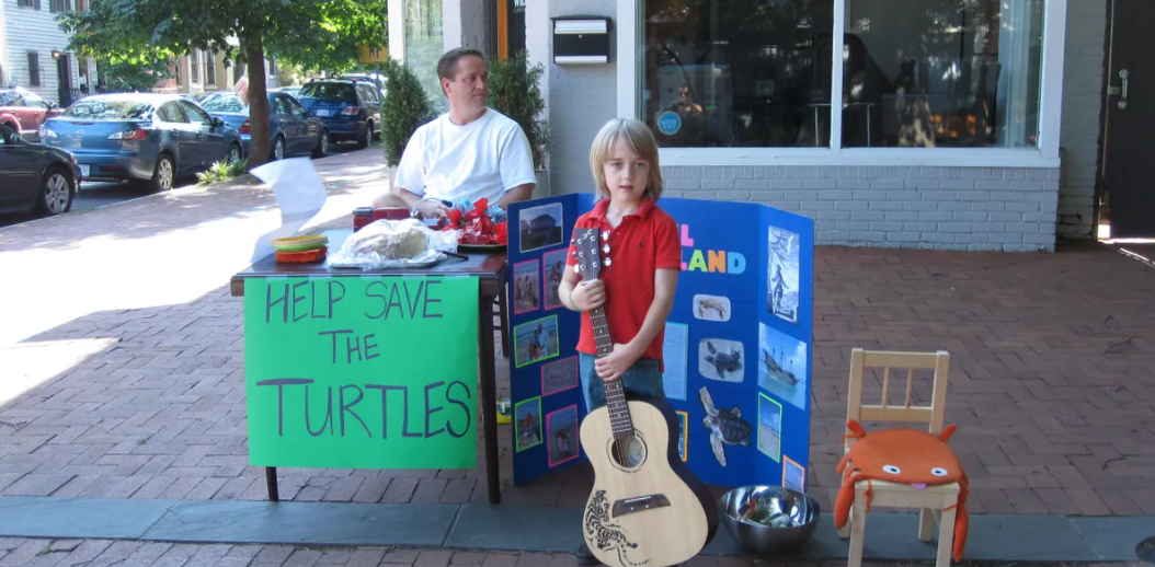 Four-year-old Grayson Houston-Henderson holding his guitar in front of a local store to fundraise. This was the first year he started raising money for sea turtles. (Courtesy of Grayson Houston-Henderson) 