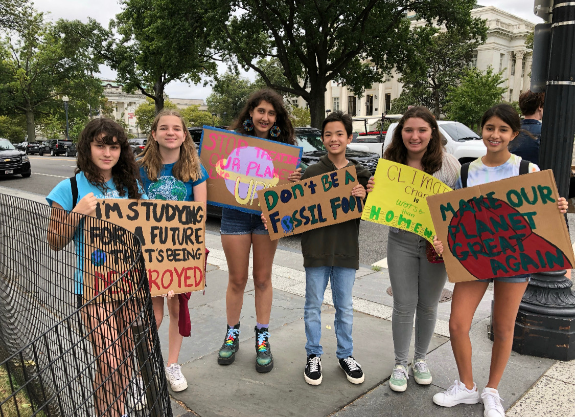 Left to right: Former student Sabine Thomas and juniors Lauren Brownell, Sophia Al-Samarrai, Braden Kiang, Madeline Robbins and Luana Dos Santos. The students are holding signs with messages against climate change. (Eliana Aemro Selassie/International Dateline)