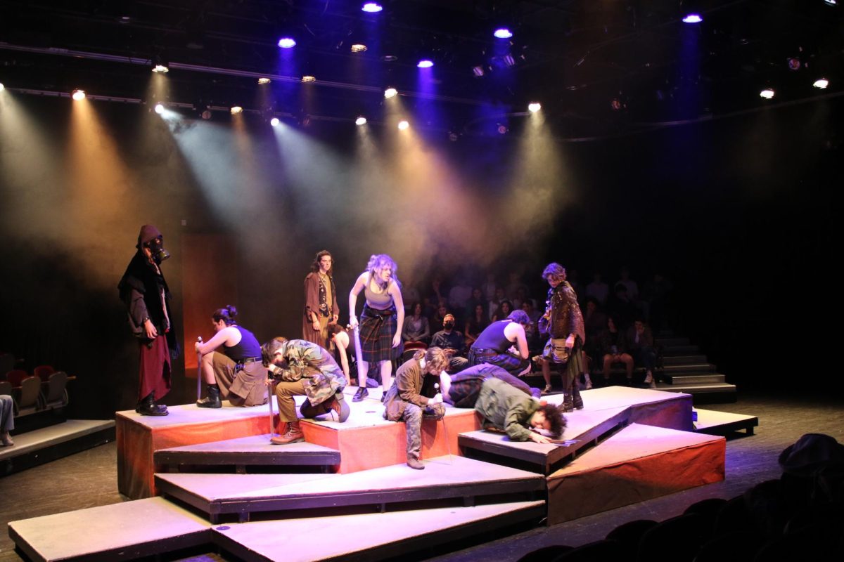The cast after a fight scene. Macbeth, played by junior Cayetana Hamilton-Garcia, stands at the center of the stage, holding a sword. The three witches, played by junior Philip Miller, junior Elia Rigolini and freshman Chiara Venturi, from left to right, circle Macbeth. (Courtesy of Cheryl Tanski)